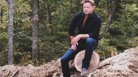 Brandon sitting on a recently-felled tree trunk, with forest in the background..