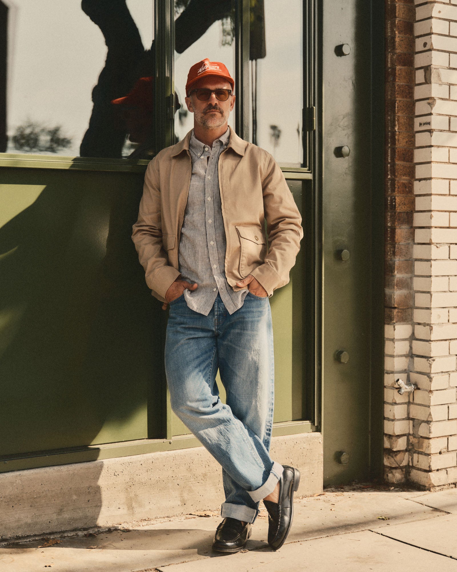fit model leaning against the wall wearing The Airman Jacket in Organic Khaki Foundation Twill, Outerwear by Taylor Stitch