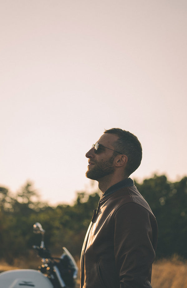 Side profile of a man in sunglasses, wearing a brown leather jacket.