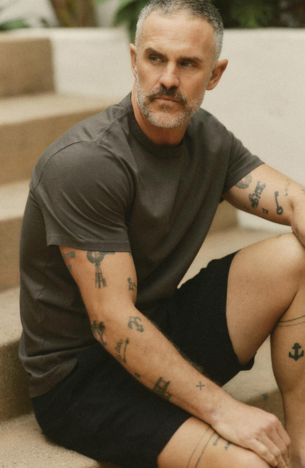 fit model sitting on a rock wearing The Organic Cotton Tee in Faded Black