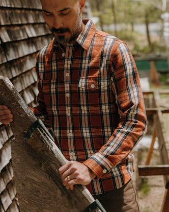 fit model holding a piece of wood wearing The Crater Shirt in Brick Plaid