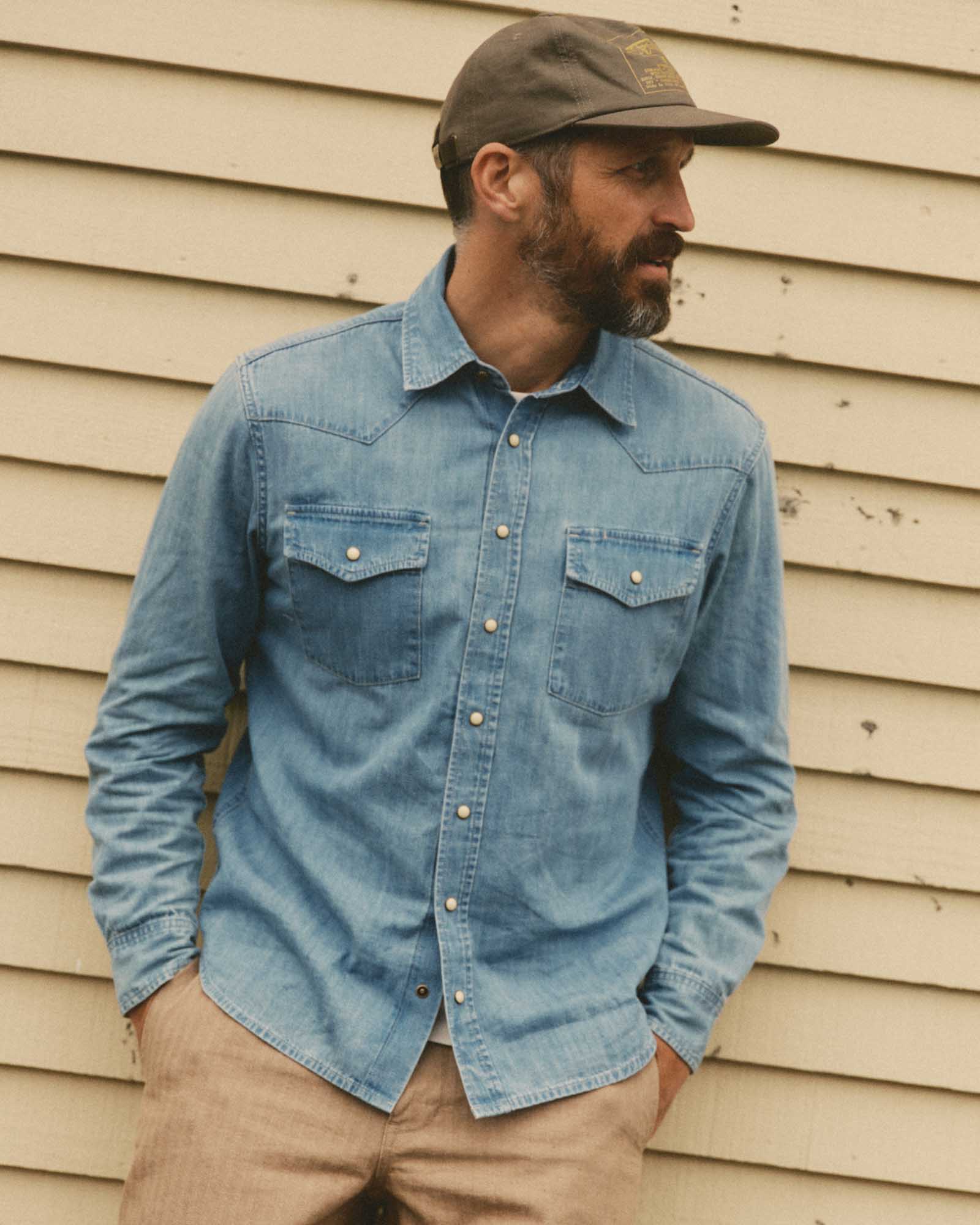 fit model leaning against the wall wearing The Glacier Shirt in Washed Indigo Denim, Wovens by Taylor Stitch