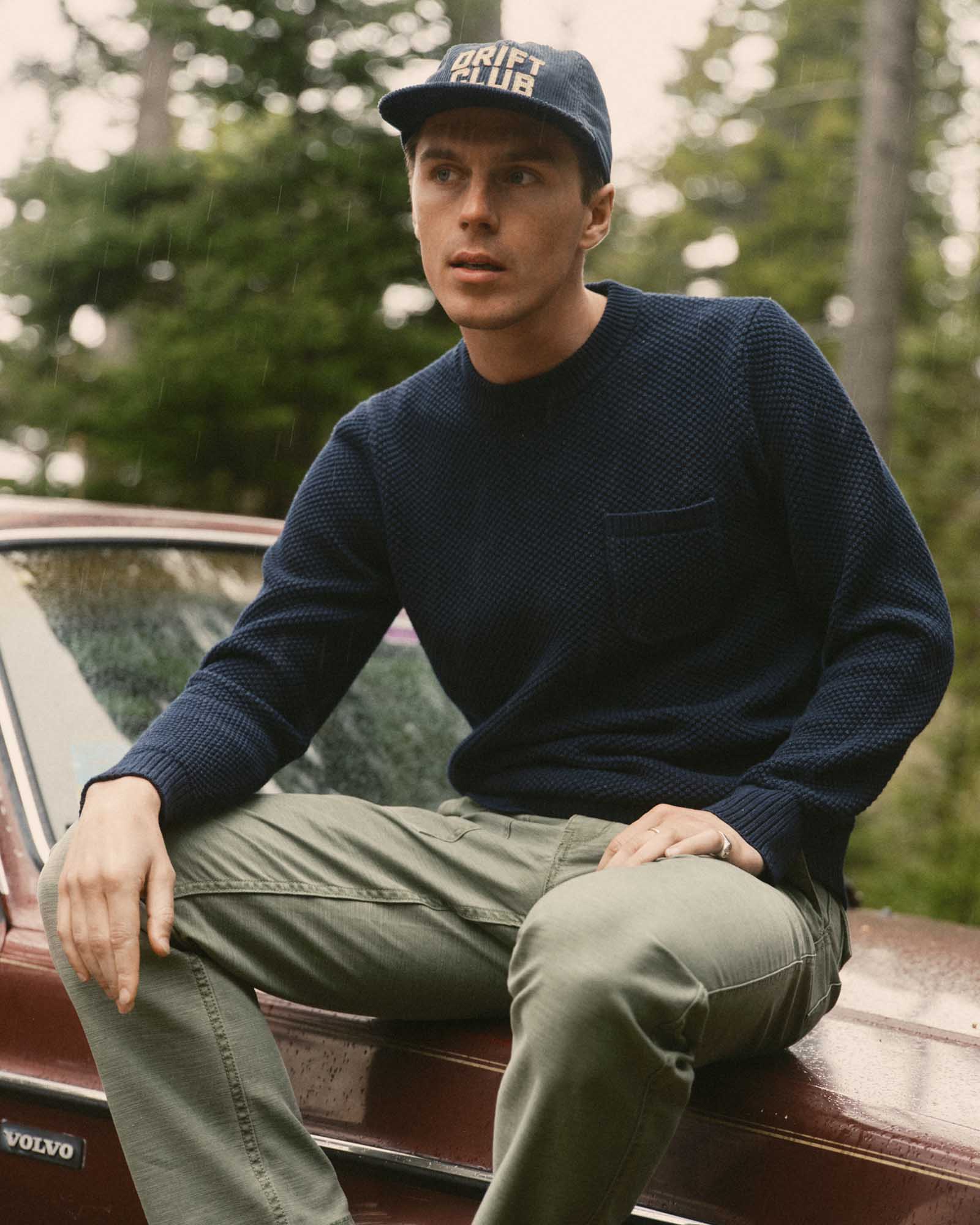 fit model sitting on a car wearing The Crawford Crew Sweater in Navy, Sweaters by Taylor Stitch