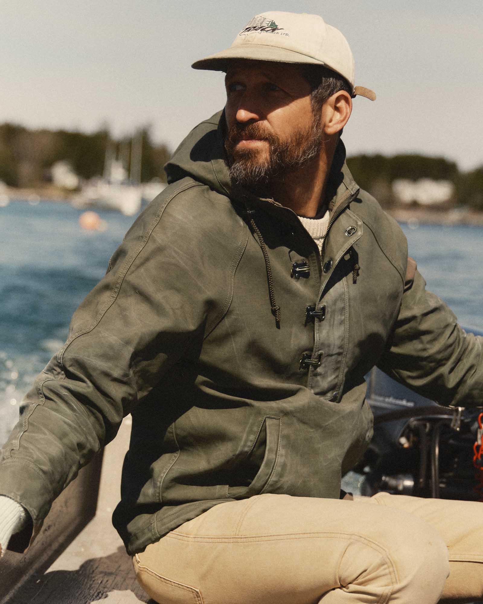 fit model sitting wearing The Hatteras Anorak in Fatigue Olive Dry Wax Canvas, Outerwear by Taylor Stitch
