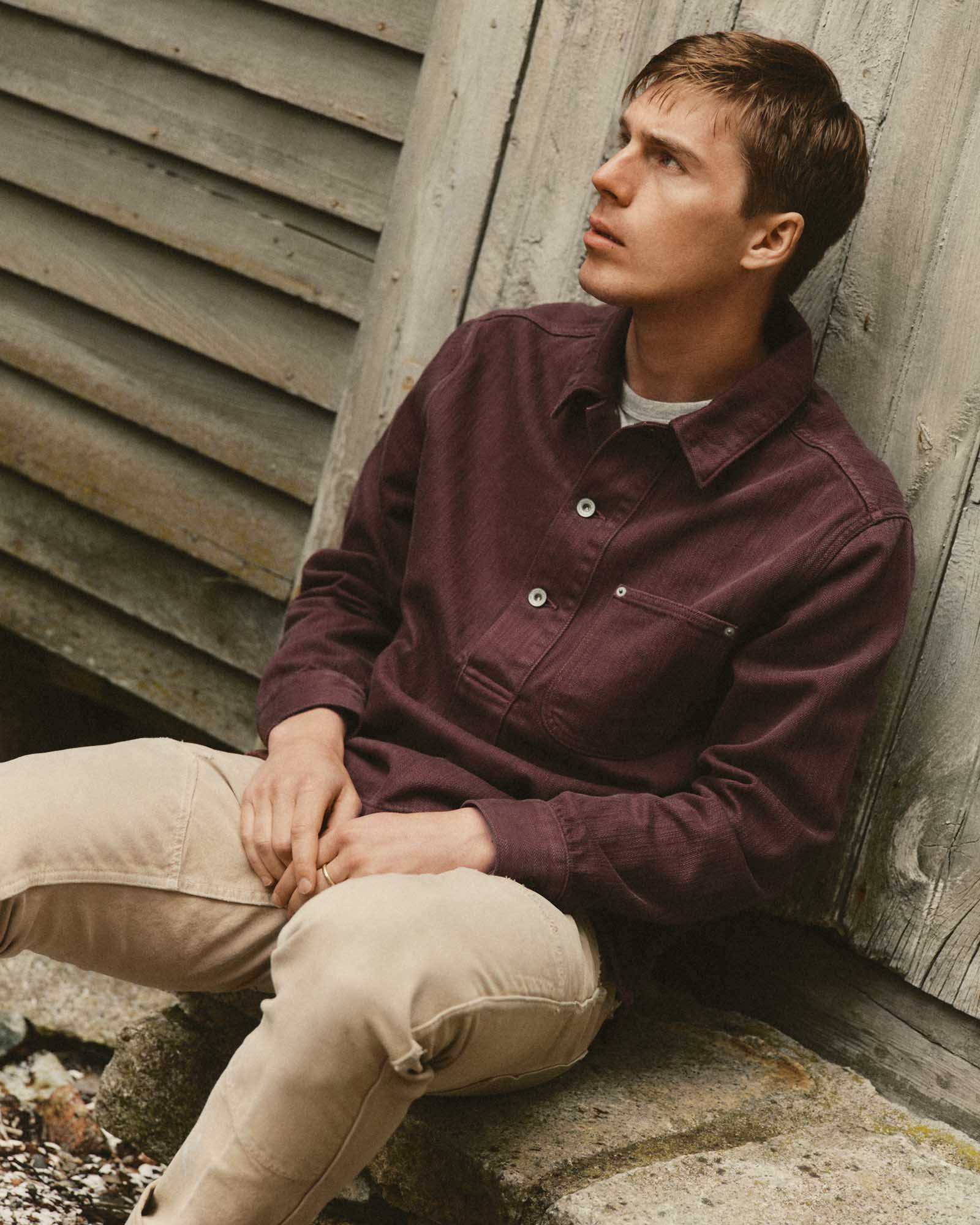 fit model sitting wearing The Milton Overshirt in Burgundy Slub Denim, Outerwear by Taylor Stitch