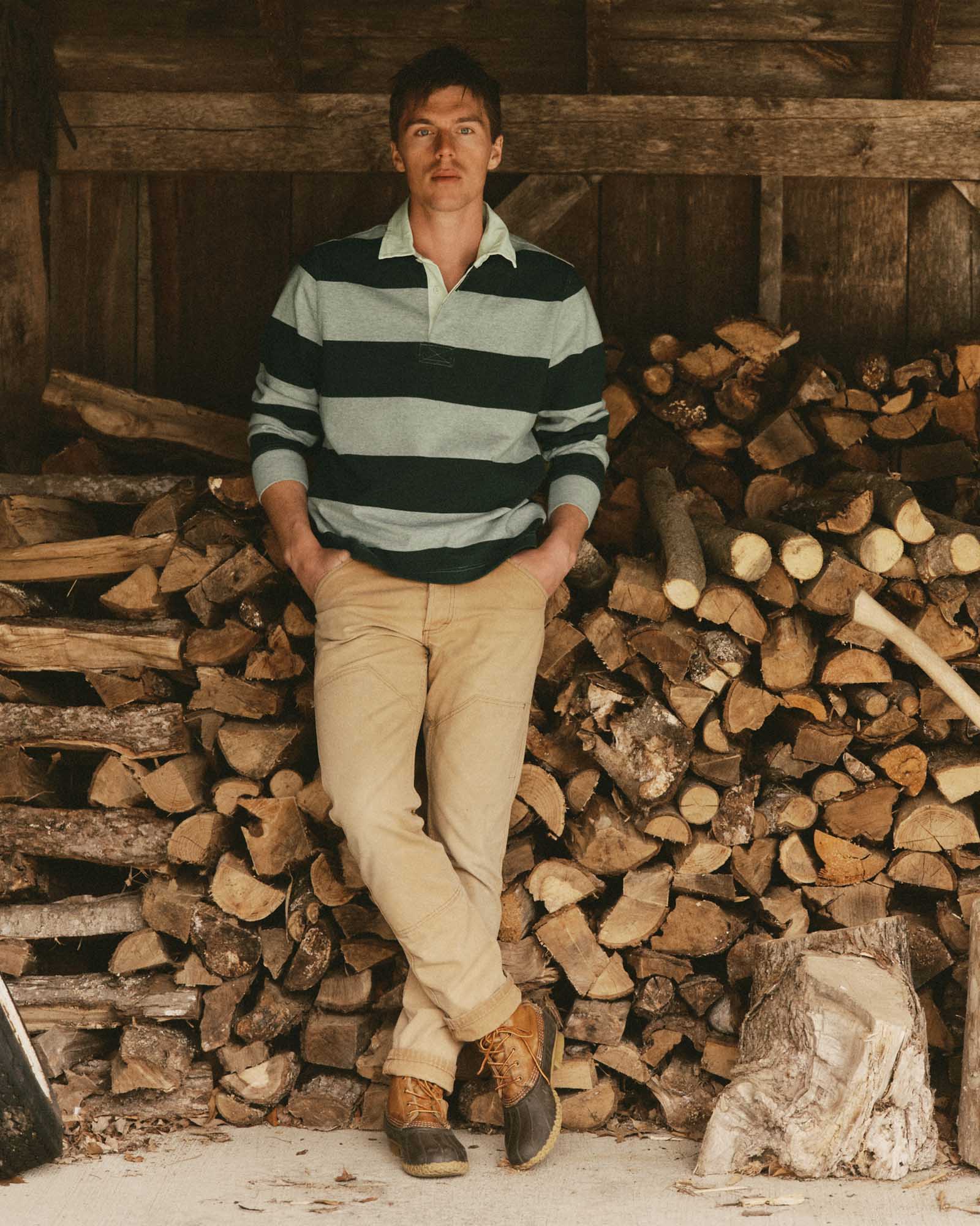 fit model leaning against the wood wearing The Rugby Shirt in Dark Forest Stripe, Knits by Taylor Stitch
