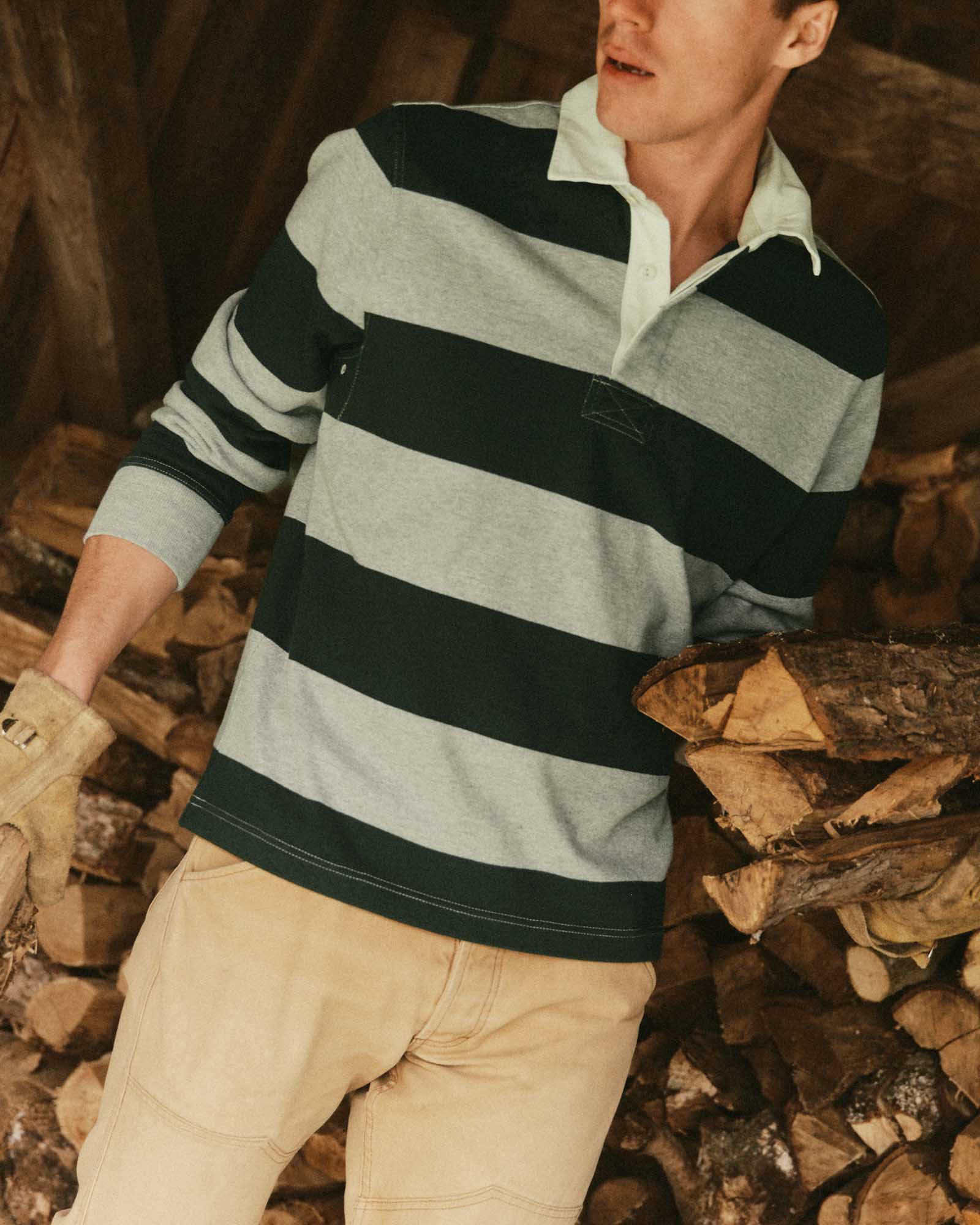 fit model holding wood wearing The Rugby Shirt in Dark Forest Stripe, Knits by Taylor Stitch