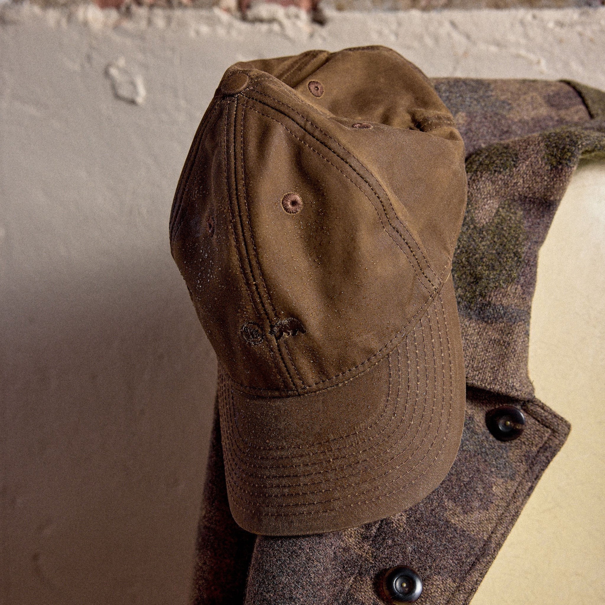 The Ball Cap in Dark Khaki Waxed Canvas hanging on a coat, Accessories by Taylor Stitch