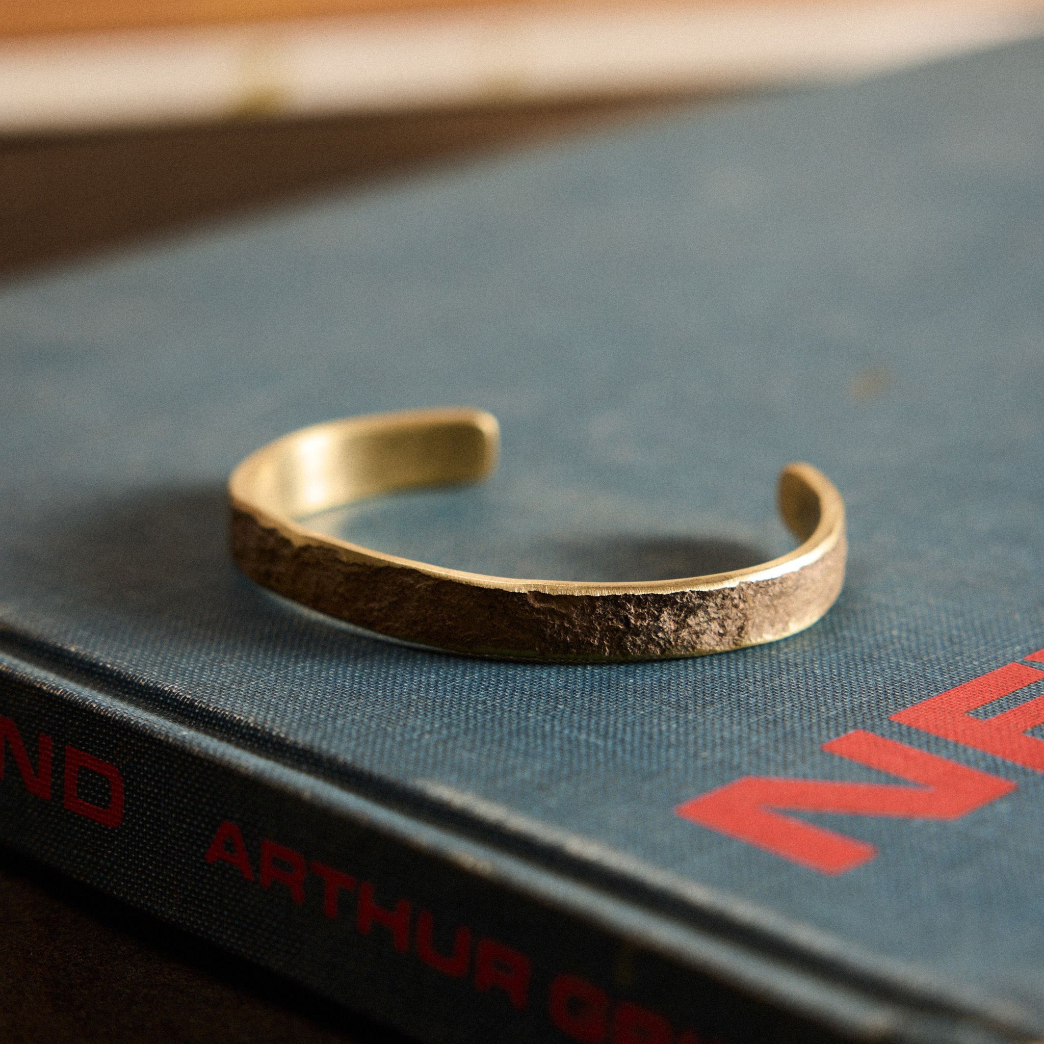 The Hammered Cuff in Brass on a book, Accessories by Taylor Stitch
