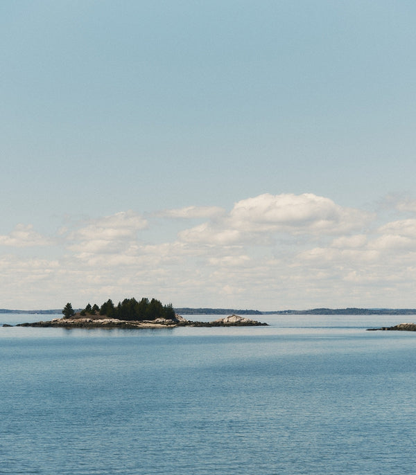 Tree-lined rocky islands across calm blue water beneath a cloudy sky